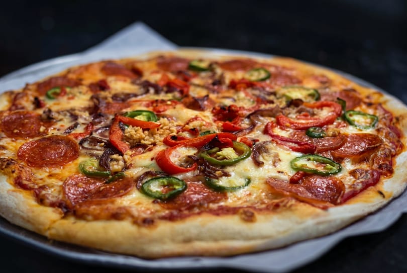 A whole pepperoni pizza with red and green peppers, and other toppings on a dark background.