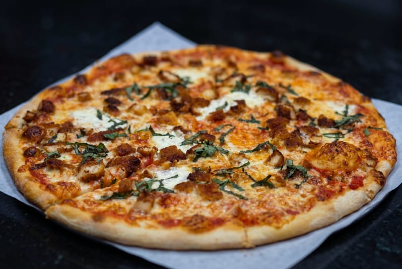 A whole pizza with melted cheese, crispy chicken pieces, and fresh basil on parchment paper.