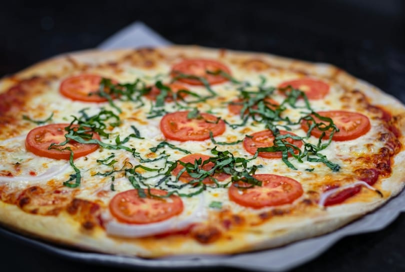 A freshly baked pizza with melted cheese, sliced tomatoes, and basil on a dark surface.