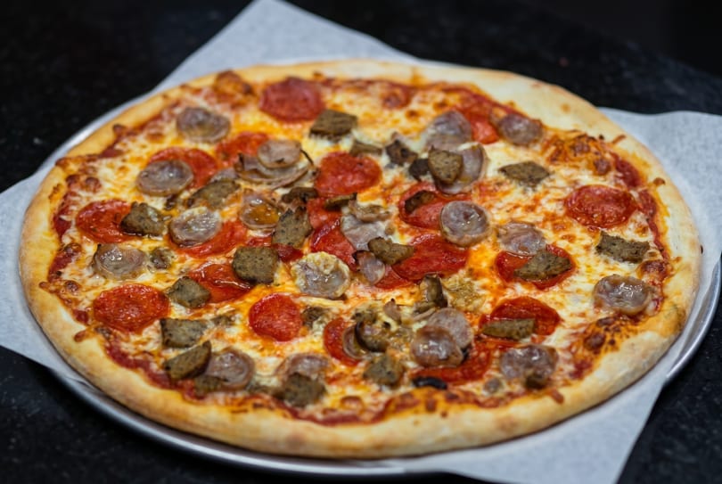 A whole pepperoni and sausage pizza on a metal tray with parchment paper.