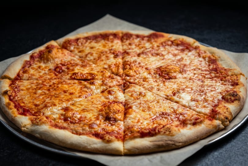 A large, cheesy pizza with tomato sauce and melted mozzarella, sliced into eight pieces on a metal pan.