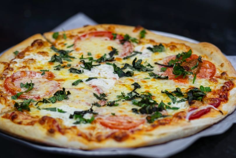 A whole Margherita pizza with melted cheese, sliced tomatoes, and fresh basil on a dark surface.