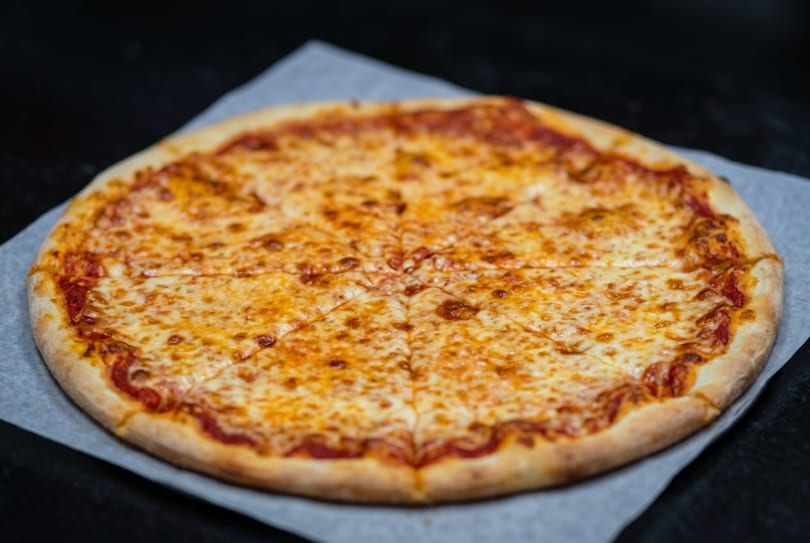 A whole cheese pizza, sliced into eight pieces, rests on parchment paper.